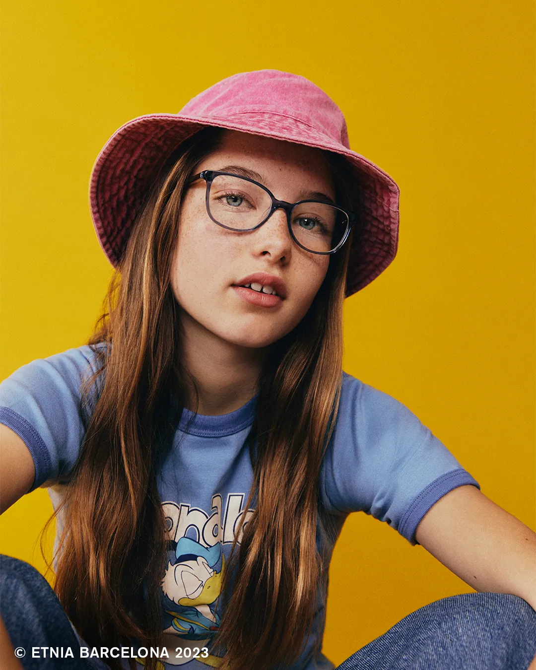 Teen in navy Etnia Barcelona glasses and a pink bucket hat, available at Boardwalk Eye Care in Cambridge, Ontario
