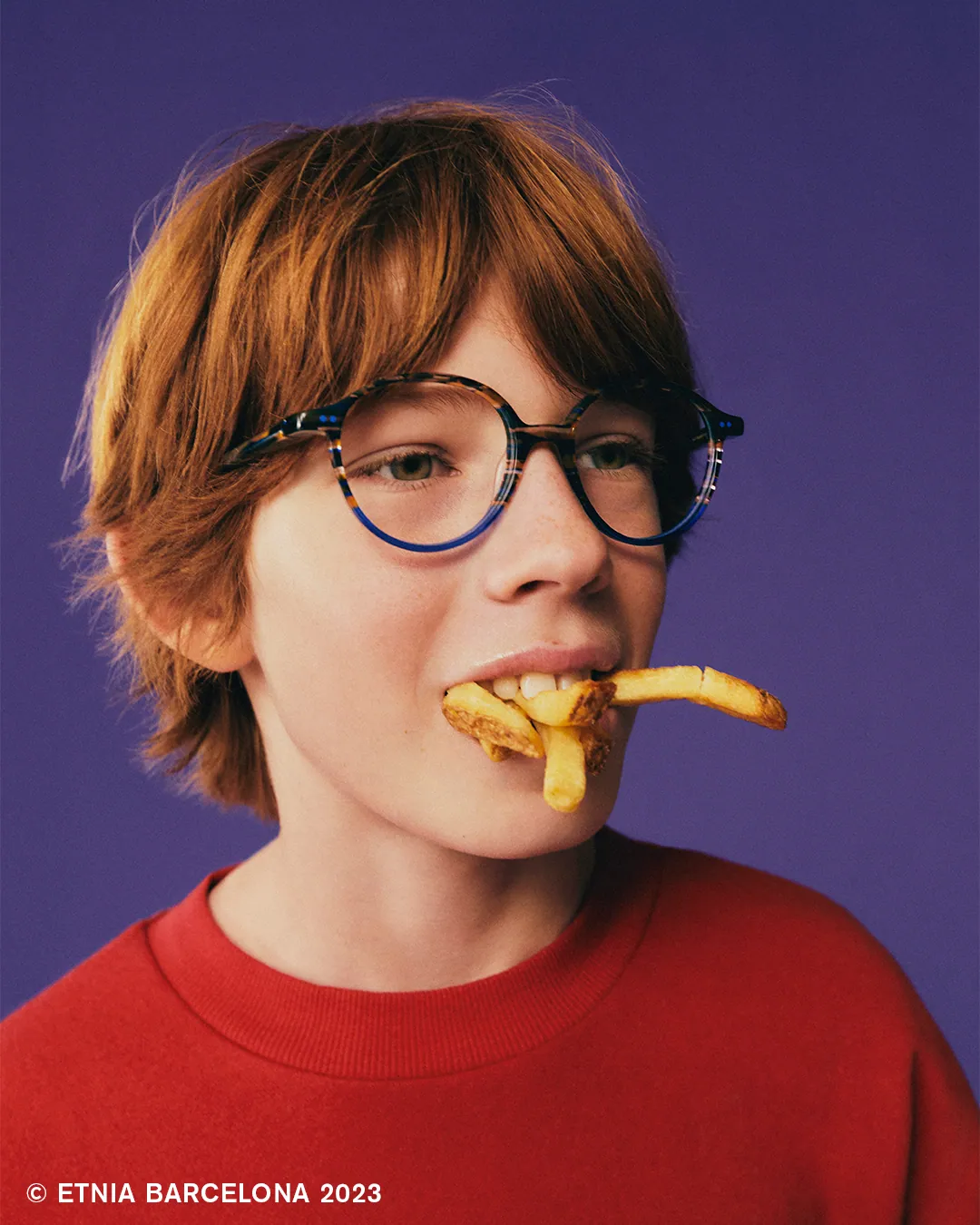 Boy eating fries while wearing patterned Etnia Barcelona kids' glasses, available at Boardwalk Eye Care in Cambridge, Ontario