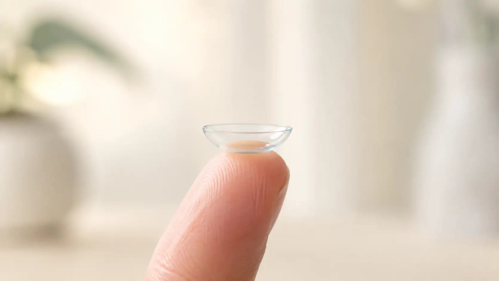 A soft contact lens balanced on a fingertip, ready to be worn